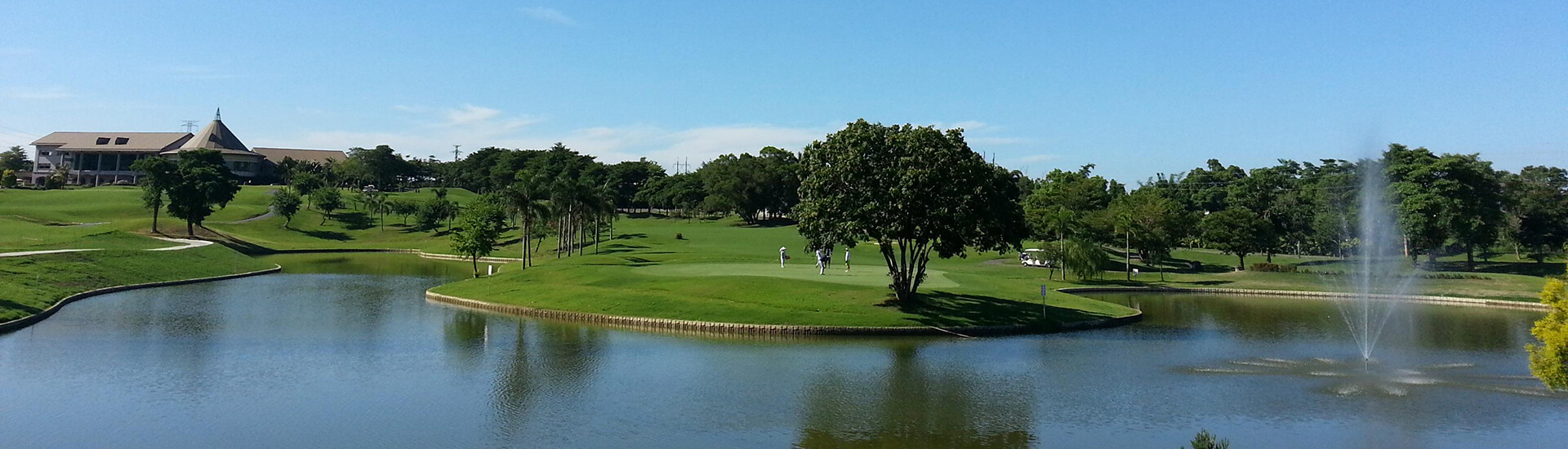 trees under a clear blue sky, with a large, calm water hazard