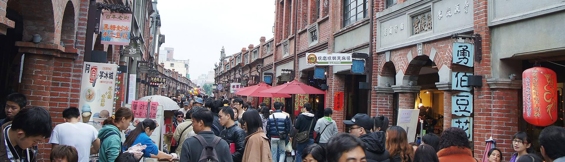 Bustling night market street filled with food stalls and bright signs.