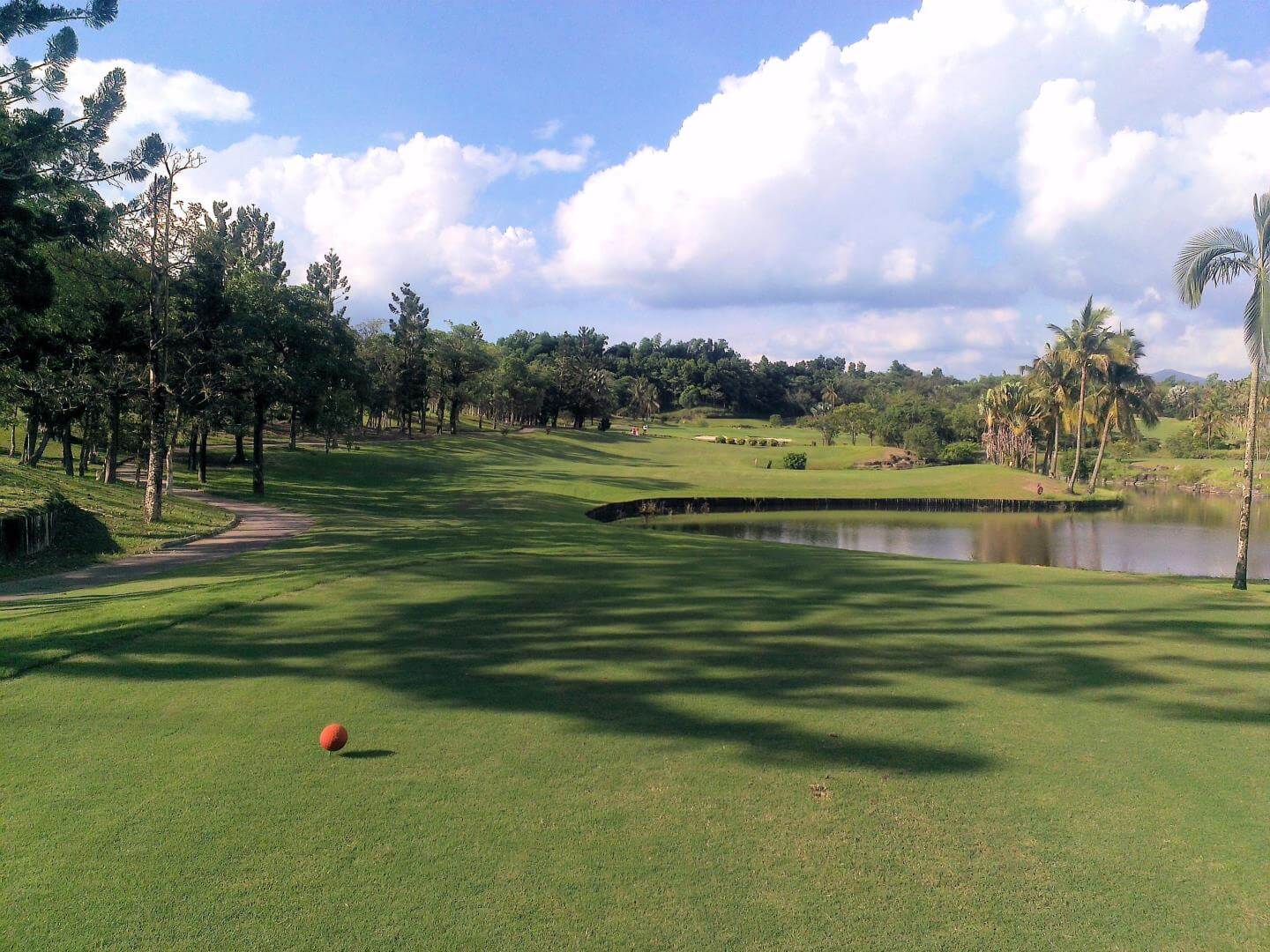 calm water hazard sits to the right, reflecting the bright white clouds above