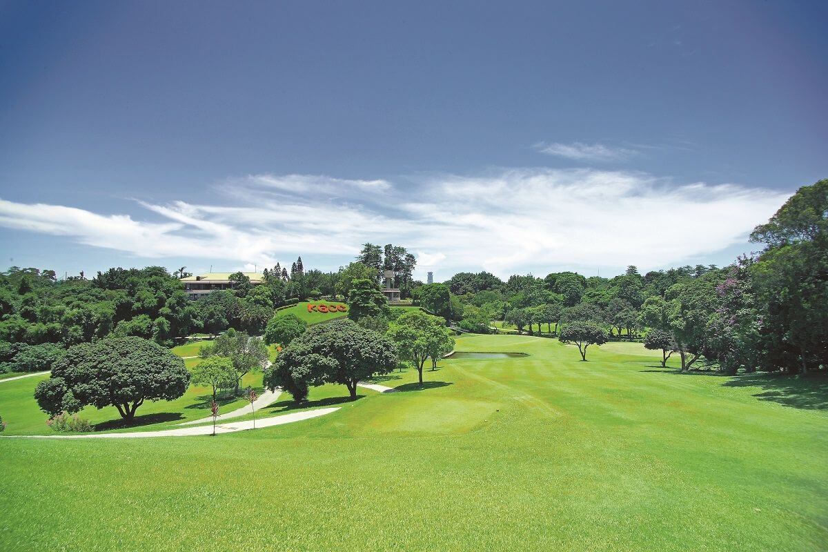 wide-angle landscape shot of a lush green golf course fairway under a blue and white sky